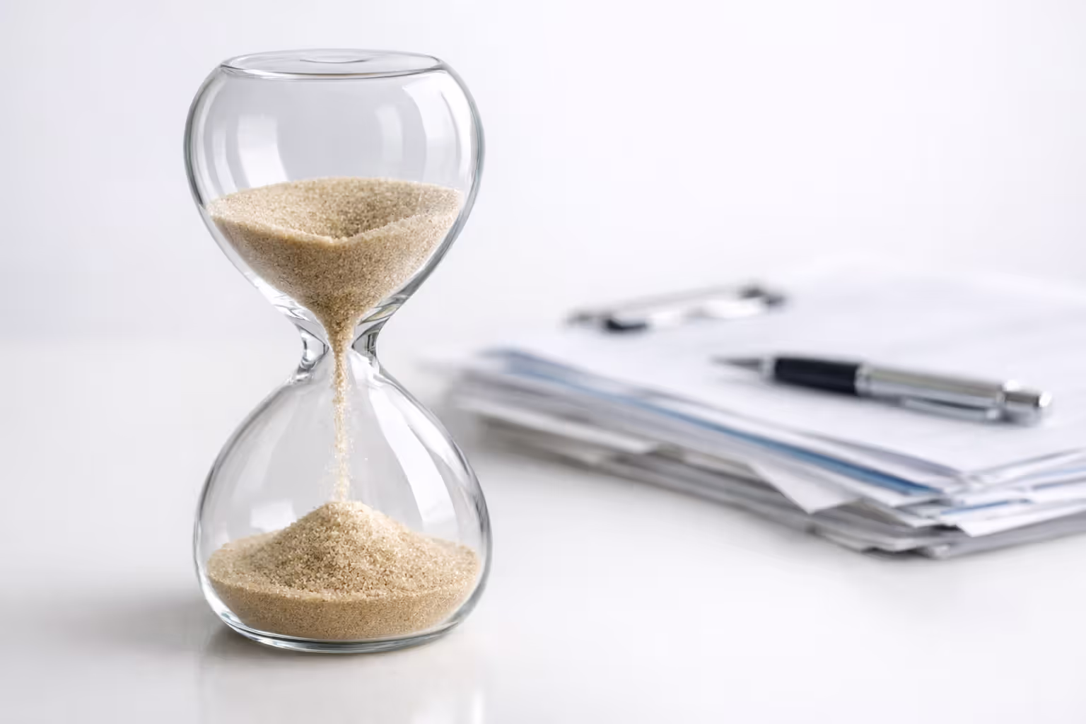Hourglass with sand flowing on a desk with blurred medical documents in the background symbolizing enrollment deadline