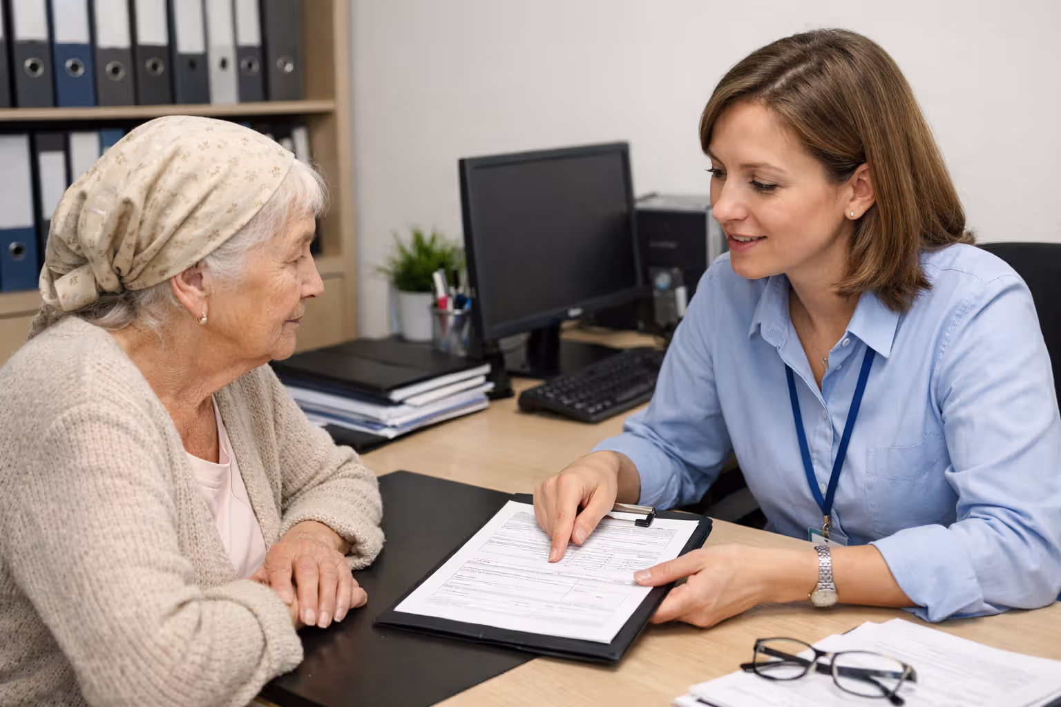 Elderly woman consulting with a social worker at an office desk about eligibility documents